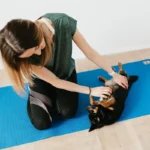 Жінка займається йогою разом з собакою на килимку