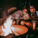 Собака з господарями біля вечірнього багаття у кемпінгу серед природи