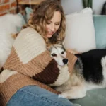 Жінка в затишному светрі ніжно гладить собаку на дивані