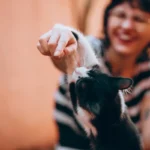 Чорно-білий кіт ласкаво треться щокою об руку усміхненої жінки, тепле домашнє освітлення