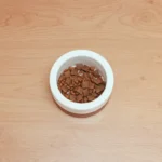 Миска з кормом для собаки на дерев'яному столі поруч зі свіжими спеціями та зеленню