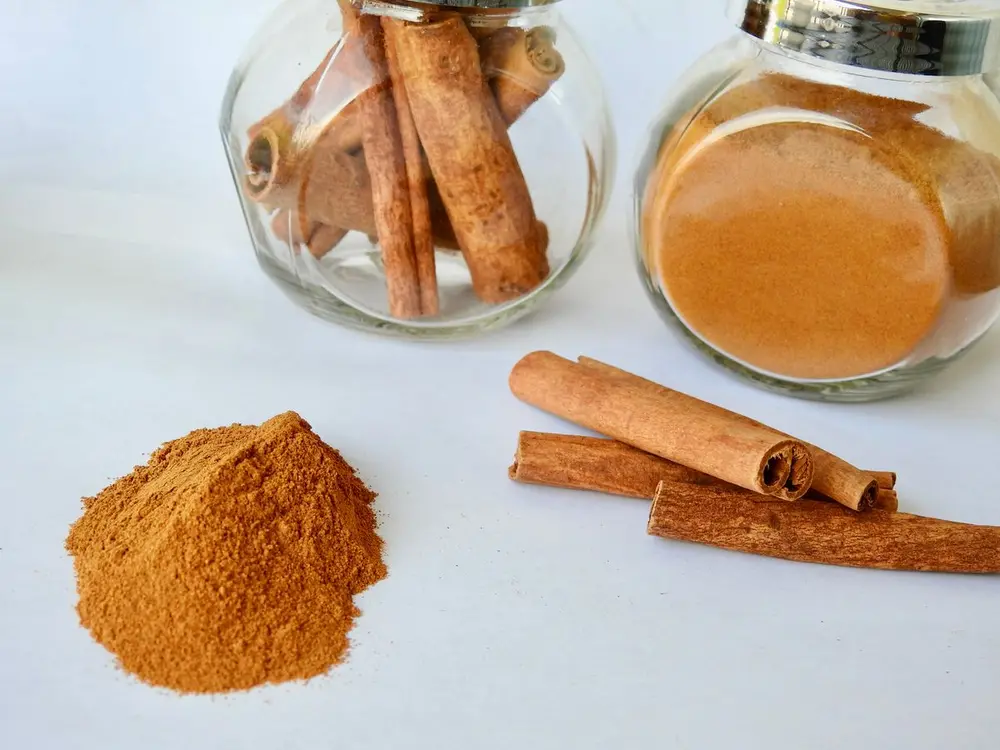 Мелена кориця і палички кориці поруч зі скляними баночками